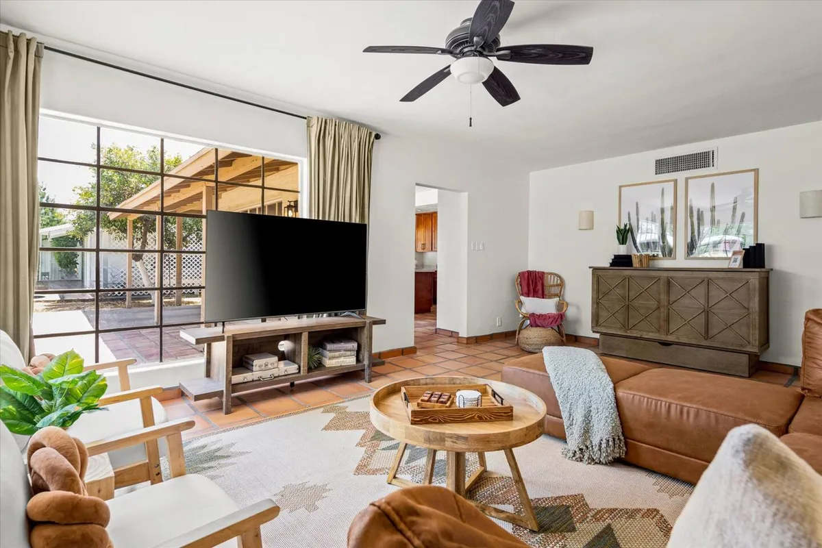 A cozy seating area centered around a comfortable sofa and a stylish TV unit, with a decorative coffee table in front. The scene is bathed in soft natural light streaming through a large window, creating a welcoming atmosphere for relaxation or socializing.