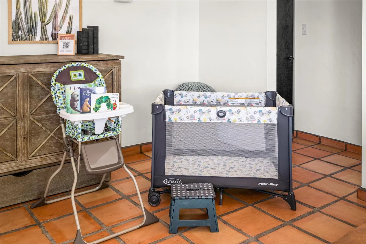 This image centers on a high chair and playpen, surrounded by decorative wall art and a wooden storage unit, creating a clearly family-oriented and child-friendly environment.