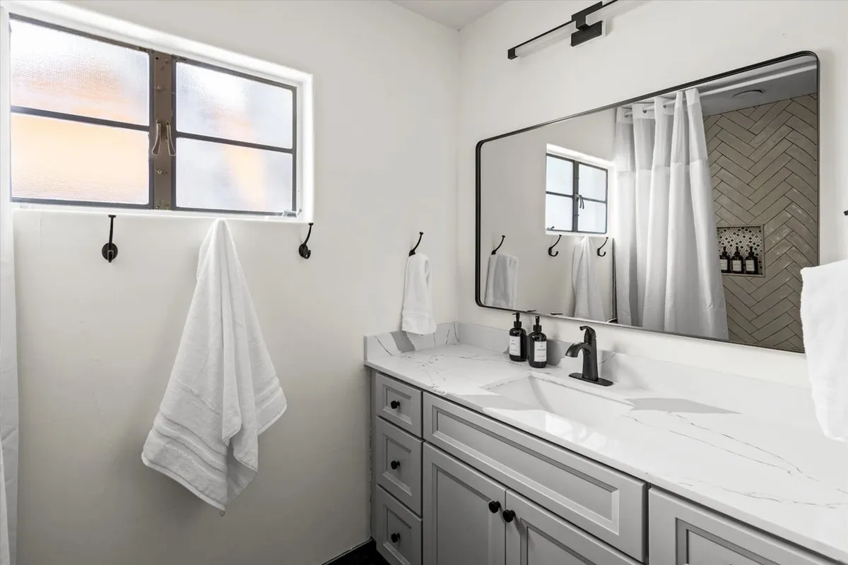 A bright, spa-inspired bathroom with a large mirror above a sleek sink, fresh towels neatly arranged, and a window allowing natural light to brighten the space. The scene suggests both morning routines and soothing evening rituals.
